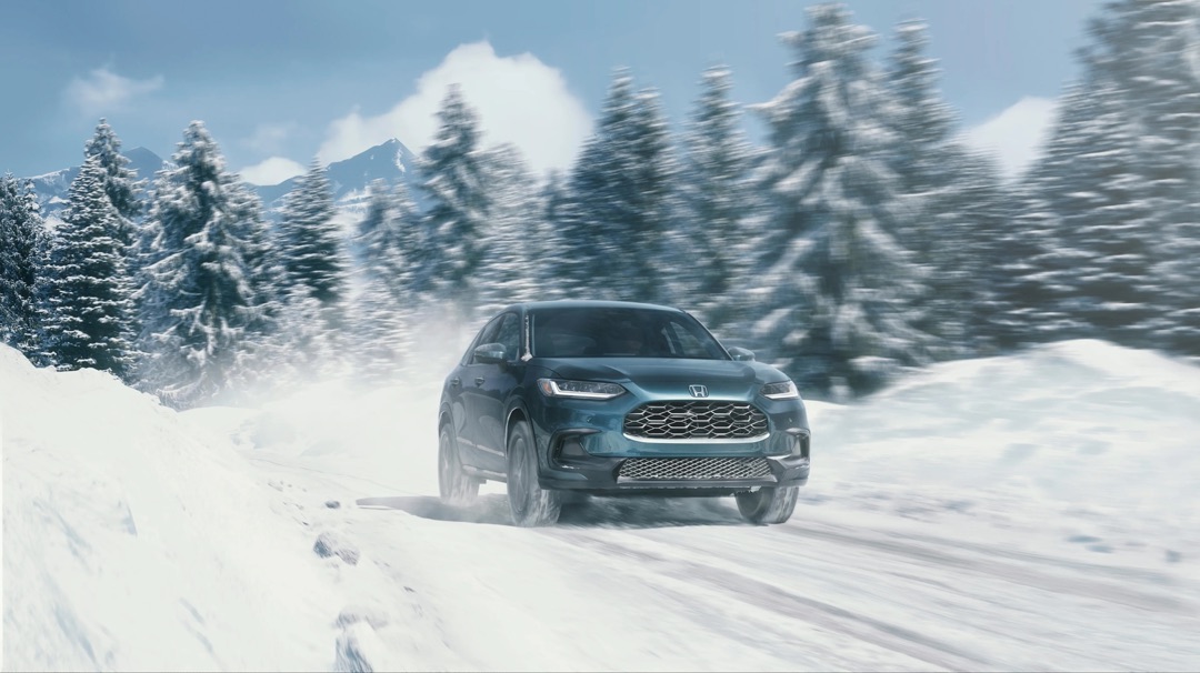 vue 3/4 avant du VUS sous-compact Honda HR-V 2023 performant sur une route enneigée en forêt